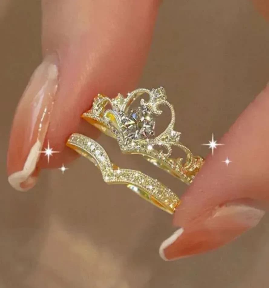 gold tone crown ring set with curved rhinestone band held between fingers