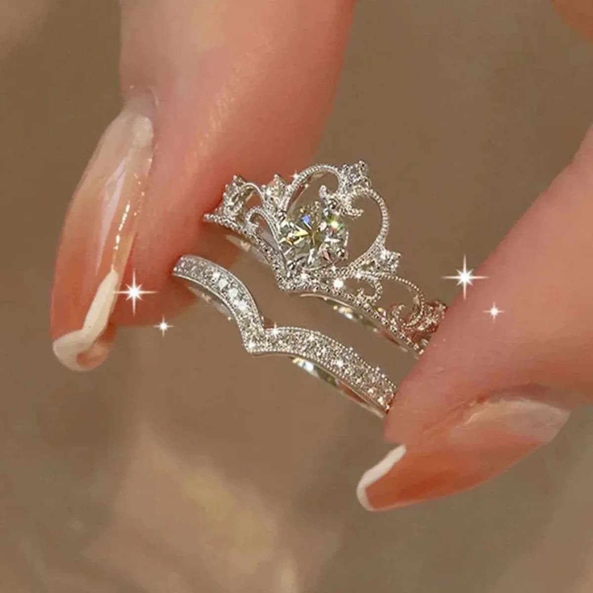 silver tone crown ring set with curved rhinestone band held between fingers